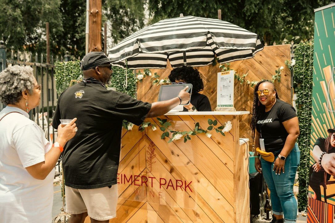 Leimert park wine booth at event. Man is checking out and paying for order