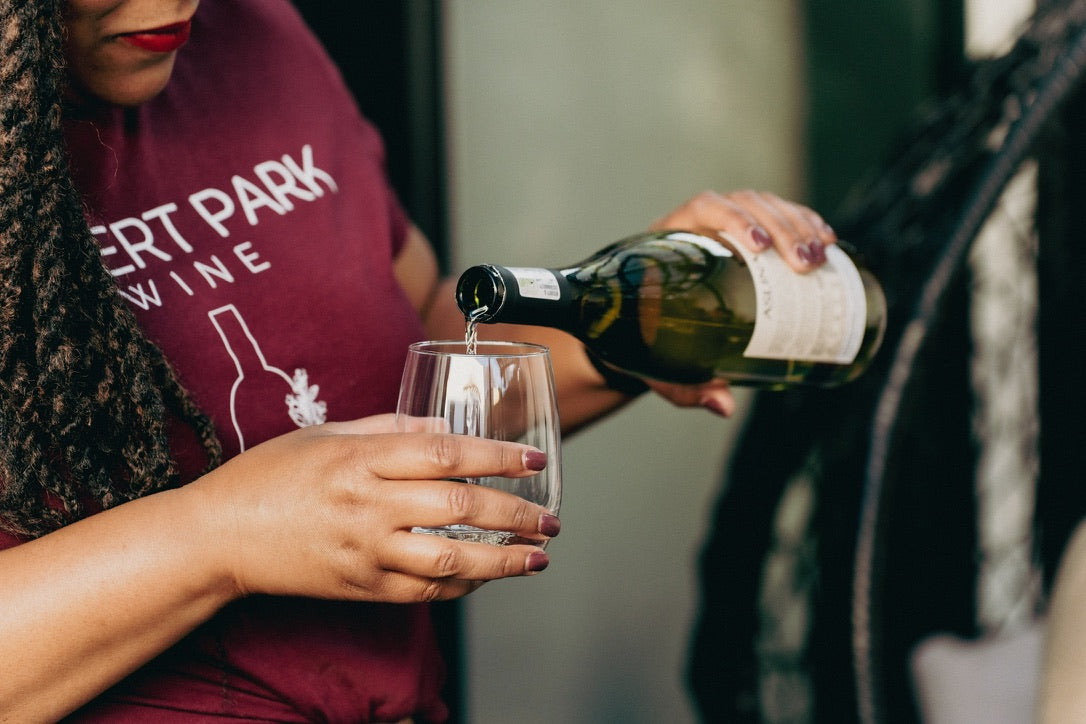 Pouring wine into short wine glass. Woman pouring the wine is wearing red shirt